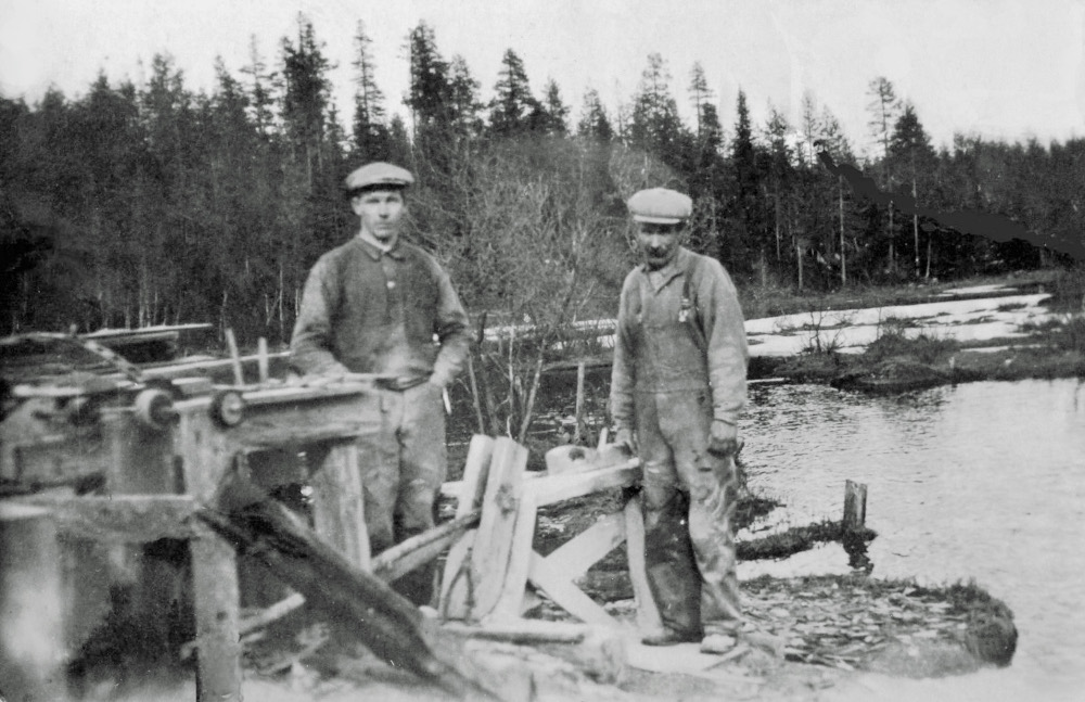 Old image of two people standing beside a whetstone planer